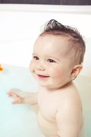 Cute baby sitting in the water, having fun and smiling while taking a bathの写真素材