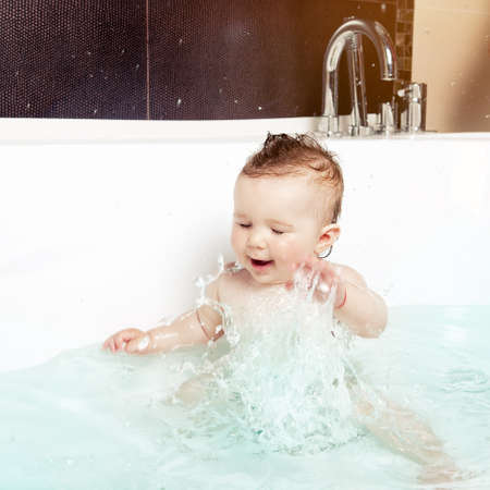 Cute baby having fun, splashing water and laughing while taking a bath in a modern bathroom interiorの写真素材