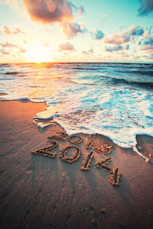  New Year 2014 is coming concept - inscription 2013 and 2014 on a beach sand, the wave is covering numbers 2013 の写真素材