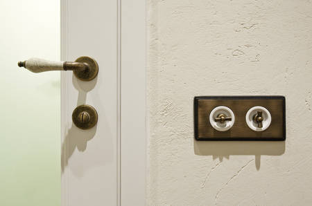 Stylish vintage brass light switchers on textured white wall and china door knob, the elements of interiorの写真素材
