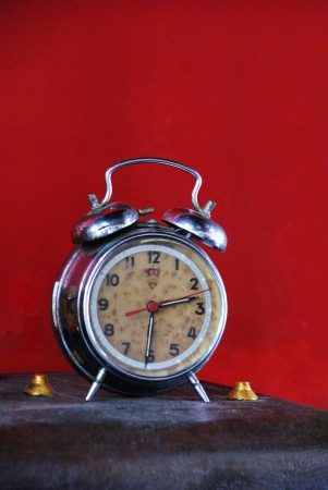 Old vintage alarm clock on table againts red wallの素材