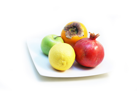 Four pieces of colourful fruits on white plate - Lemon, Granny Smith Green Apple, Pomegranate, Hachiya Persimmonの写真素材
