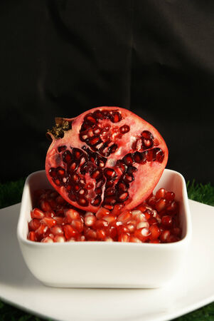 Half cut open ripe and juicy Pomegranate fruit or Buah Delima with broken loose pieces in a white square bowlの写真素材