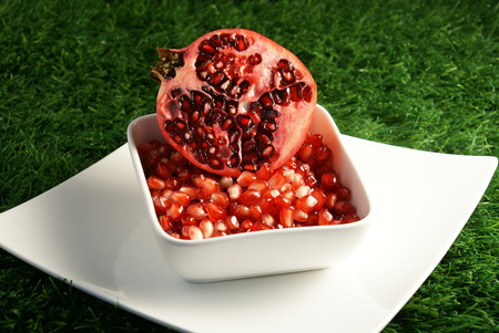 Half cut open ripe and juicy Pomegranate fruit or Buah Delima with broken loose pieces in a white square bowlの写真素材