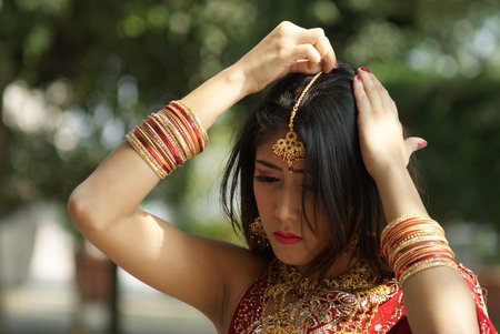 Young Indian girl in red traditional saree clothing fixing her hair pin