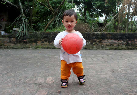 HAI DUONG, VIETNAM, September, 2: Asian boy about 1 year old, play football alone in the yard on September, 2, 2013 in Hai Duong, Vietnam.のeditorial素材
