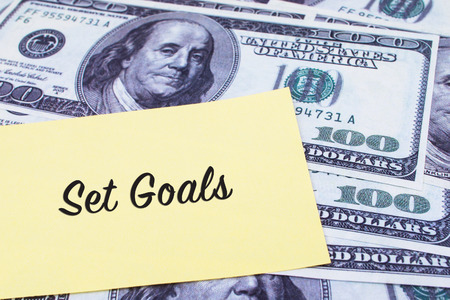 Focus on the words Set Goals written on a yellow paper with USD dollars currency as a background. Concepts of investment and business.の写真素材