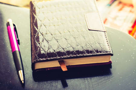 Purple notebook and pen lying on a black table lit by bright sunlightの写真素材
