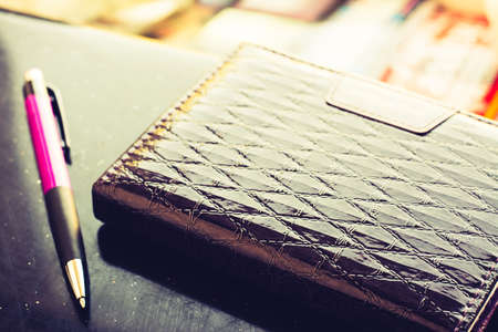 Purple notebook and pen lying on a black table lit by bright sunlightの写真素材