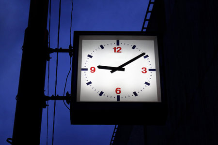 Street clock with backlit on a lamppost in the night city