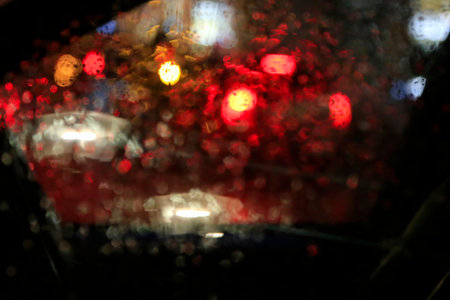 The lights of the big city at night through the glass of the car covered with raindrops, blurred...