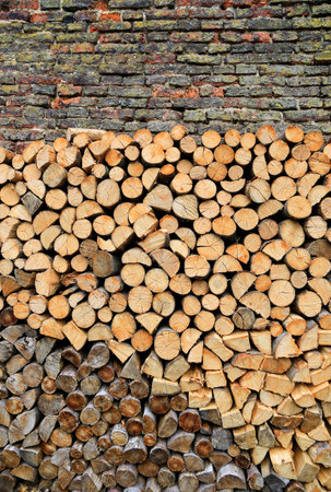 Stack of firewood on a old weathered brick wall background, close-up texture
