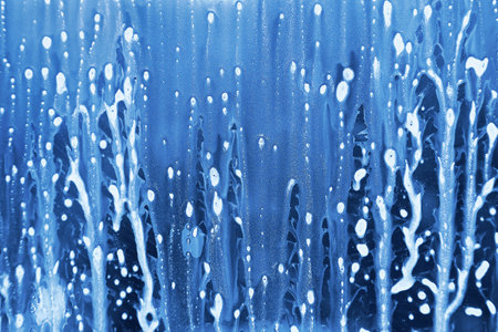 Blue background with soap foam flow on the glassの写真素材