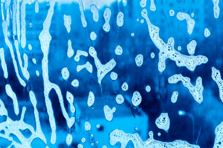 Blue background with natural soap foam pattern on the glassの写真素材