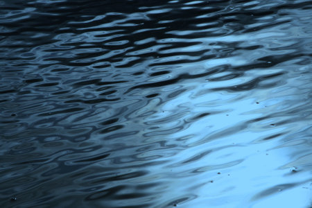 Dark blue wavy water surface with light glare, closeup natural backgroundの写真素材