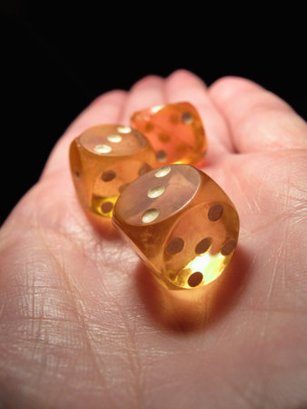 Hand holding three old dice on a black background, closeup