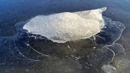 Block of ice on the surface of a frozen river in sunlight, close-up natural background