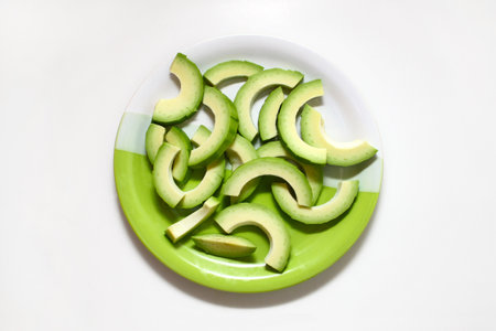 Avocado cut into slices on a plate isolated on white backgroundの写真素材