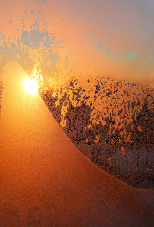 Beautiful sunrise and ice patterns on winter window pane, close-up of natural textureの写真素材