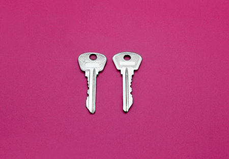 Two silver keys to english lock on bright crimson paper backgroundの写真素材
