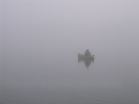 Lone fisherman with a fishing rod in a boat on the river in a fogの写真素材