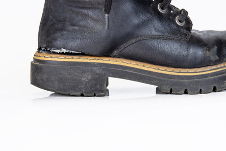 Closeup detail of one black worn ankle leather combat boot with thick, sturdy sole and laces. Single...