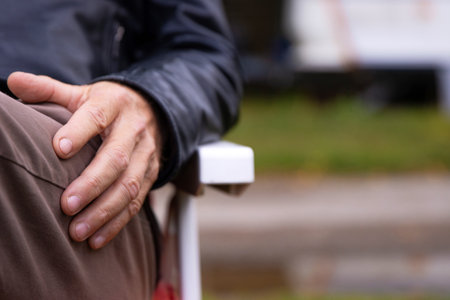 Mature elderly man resting outdoors. Senior person in his sixties sitting on a chair. Camping lifestyle of a retired male. Closeup of an older man  hand on his lap. Selective focusの写真素材