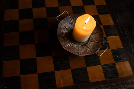 Lit candle on the wooden chessboard. Burning candle on the wooden table in the candleholder. Burning...