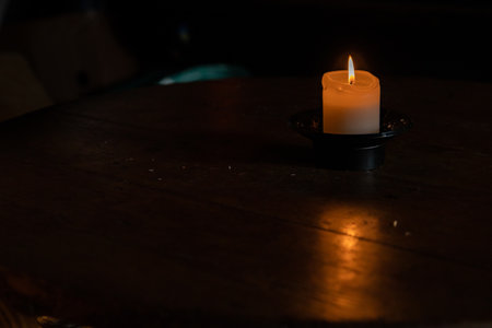 Beautiful burning wax candle with the flame reflection on the wooden table. Dark background with turquoise and blue reflex. Minimalistic concept. Graphic design, poster. Copy text space. Bokeh effectの写真素材
