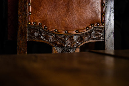 Close up of the detail of antique wooden Chair covered with brown leather upholstery, decorated with metal rivets and artistic wood carving elements. Dark background. Copy Space.の写真素材