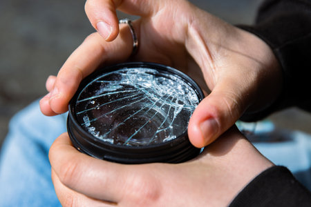 Photographer unscrewing broken lens filter from DSLR photo camera with after if fall down onto the floor. Close up. Destroyed cracked glass of photo-filter. Macro. Top view. Selective focus.の写真素材