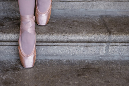 Closeup of ballerina's pointes on the gray stone steps background. Dance sitting on the steps. BallerinaÂ´s feet with pink ballet slippers on. Minimalistic, simple. Copy space.の写真素材