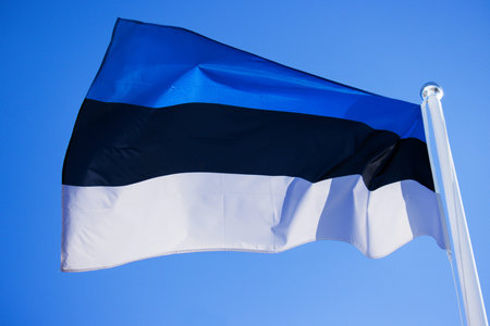 Beautiful flag of Estonia waving in the wind on the flagpole against blue sky with clouds. Close up...