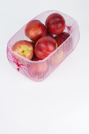 Plastic container of nectarines covered with red mesh. Fresh juicy nectarines in plastic package isolated on white background. Empty copy space. Selective focusの写真素材