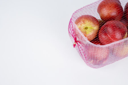 Plastic container of nectarines covered with red mesh. Fresh juicy nectarines in plastic package. Empty copy space. Selective focusの写真素材