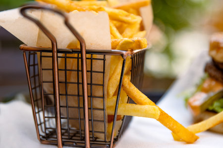 Close up view of golden, crispy French fries served in a stylish wire basket lined with brown...