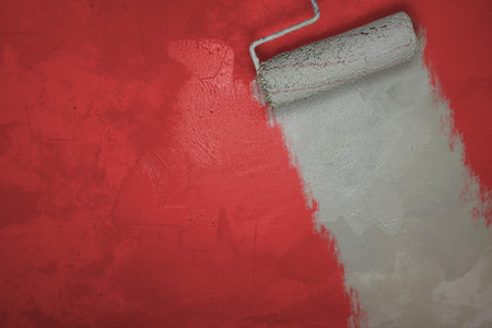 Painting wall with with roller brush into red white colors. Home renovation concept. Renovating apartment. Textured background, place for text. Simple minimalist design. Close up. Empty copy spaceの写真素材