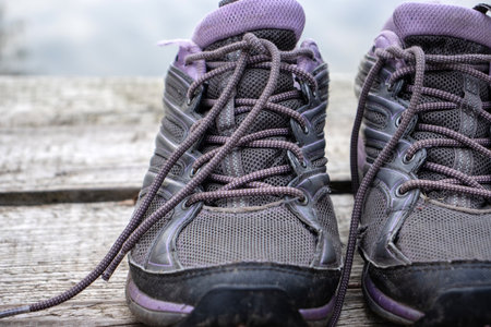 Worn out pair of running sport shoes on a old wooden deck floor on the lake beach. Autumn cloudy day in nature. Active lifestyle, running, marathon concept. Close up, copy space, selective focus.の写真素材