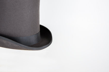 Magic hat. Topper. Elegant vintage gray beige wool felt top hat with black band on the wooden hat block. Grosgrain ribbon trim around rolled brim. Isolated on white background. Close-up. Copy space.の写真素材