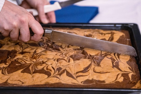Woman cutting tasty marble pie with a big knife on black baking tray. Cutting a piece of a delicious...