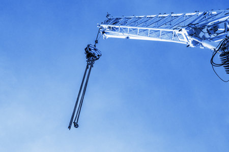 Construction crane arm with hook with cable against clear blue clear sky background. Industrial equipment or tools. Looking up at the sky. Industrial landscape. Copy space. Selective focus.の写真素材