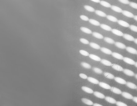 Blurred light spots, shadows from the blinds on the concrete wall on a sunny day, interior design. Abstract background, pattern, texture concept. Gray, white colors. Copy space.の写真素材