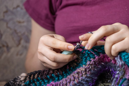 Young lady crocheting holding crochet hook and wool thread in her hands, creating handmade cloth,...