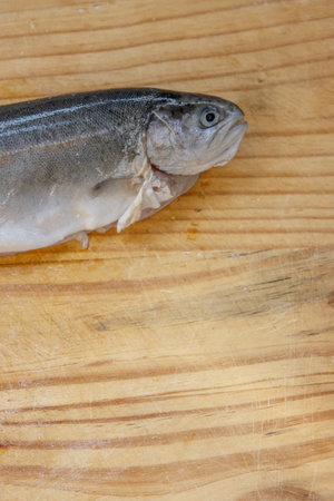 Carving big raw fresh trout on the old wooden cutting board. Cooking whole freshwater rainbow trout. Oncorhynchus mykiss on the chopping plate. Wooden background. Close up. Copy space. Macro. Top viewの写真素材