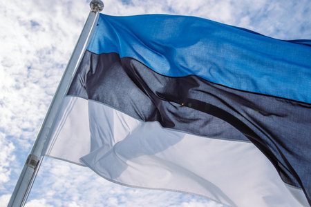 Beautiful flag of Estonia waving in the wind on the flagpole against blue sky with clouds. Close up of Estonian national flag fluttering on windy day. Cloudy sky background. Copy space.の写真素材