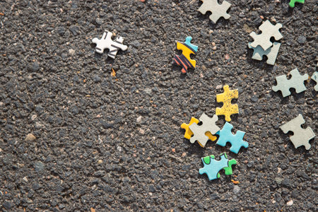 Few pieces of mixed jigsaw puzzles set scattered on the gray asphalt pavement on the street. Messy chaotic concept. Abstract background. Copy space. Close up. Selective focus. Blurred.の写真素材
