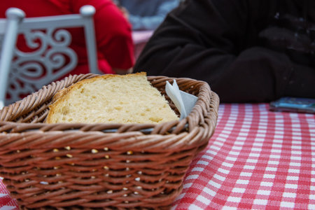 Slices of white bread in the basket on the table with white red checkered tablecloth. Table outside...