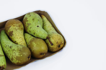 Pile of green ripe pears packaged in rectangle cardboard container for retail sale, isolated on...
