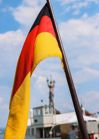Flag of Germany on the ship waving in the wind over the Constance lake (Bodensee). German national flag on a boat. Blurred Statue Imperia, tourist ship, blue sky, white clouds. on the background,の写真素材