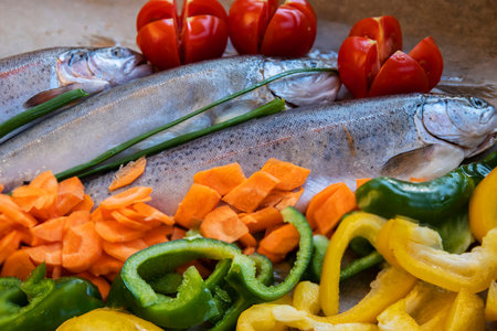 Beautifully arranged fish with seasoned vegetables, including tomatoes, potatoes, and peppers, ready for cooking on a tray, creating a vibrant, healthy dishの写真素材